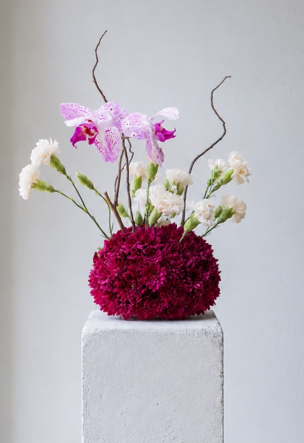 Arreglo floral escultórico con orquídeas, claveles y crisantemos vino sobre un pedestal, diseño floral para eventos de Roses for Rosie